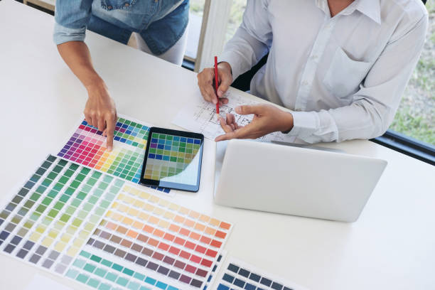istock Two young interior design or graphic designer working on project of architecture drawing with work tools and color swatches, colour chart in digital tablet at workplace 912254762