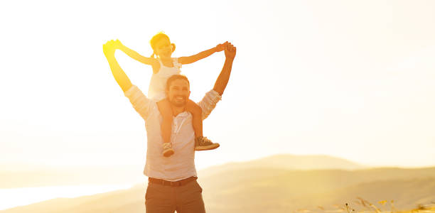 istock father's day. child daughter sits on her dad shoulders outdoors on a summer 912260118