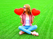 Young woman kisses an air red balloon in the shape of a heart on the grass