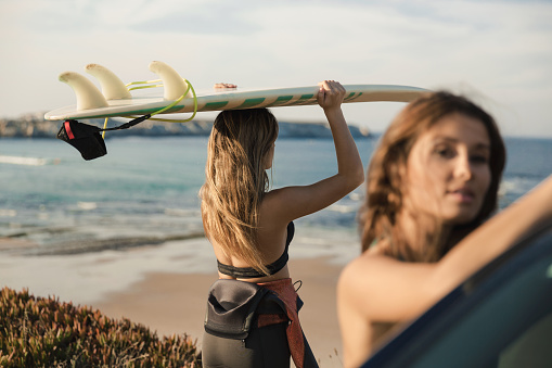 Two beautiful surfer girls near the coastline and one of them checking the waves