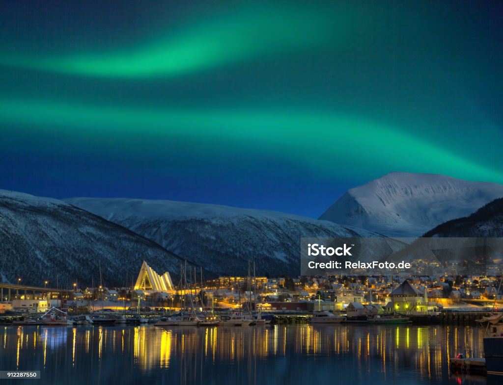 View at night on illuminated Tromso city with cathedral and majestic aurora borealis Tromso Stock Photo