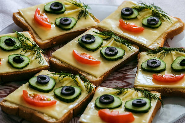 Funny smiling sandwiches with face from cucumbers, tomato, olive and dill. Perspective view with selective focus.