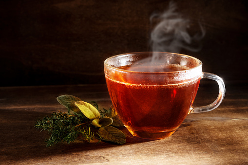 tea freshly brewed in a glass cup and some herbs on a dark rustic wooden background, healthy hot drink against cold and flu, copy space, selected focus