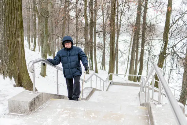 An elderly retired man with a wand climbs the marble staircase in the park. Holds on the railing. Street, day, Moscow, Tsaritsyno.