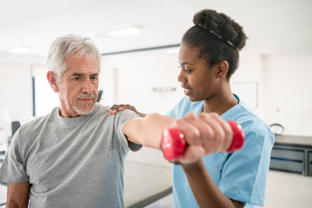 physiotherapeuten, die ihre senior patientin mit seiner schulter haltung zu korrigieren, da er freie gewichte hebt - physical and occupational therapists stock-fotos und bilder