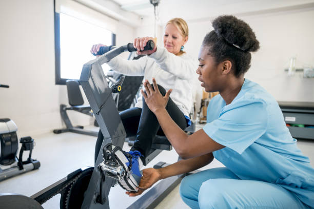 afrikanische amerikanische ergotherapeutin einem patienten erläutert, das statische fahrrad verwenden - physical therapy exercise machine exercising exercise equipment stock-fotos und bilder