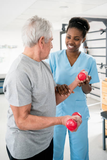 istock Black occupational therapist helping a senior patient with his free weights workout 912333750