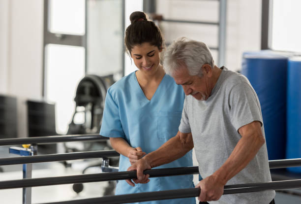 Physiotherapist helping a senior patient while he walks using his hands to support his weight on the bars Physiotherapist helping a senior patient while he walks using his hands to support his weight on the bars and therapist looking very happy occupational therapy photos stock pictures, royalty-free photos & images