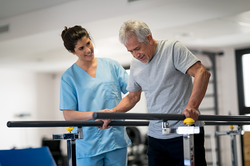 Occupational therapist and senior patient working out using parallel bars to walk both looking very happy and smiling