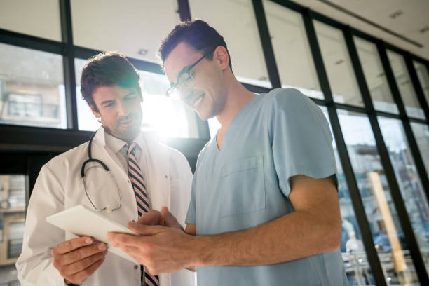 мужской медсестра и врач, глядя на медицинскую карту на планшете как выглядит счастливым - male nurse male healthcare and medicine technician стоковые фото и изображения