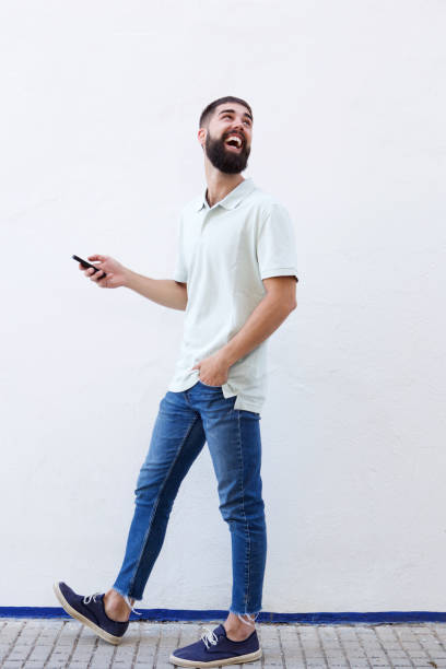 istock Full length laughing man with beard walking and holding cellphone 912334296