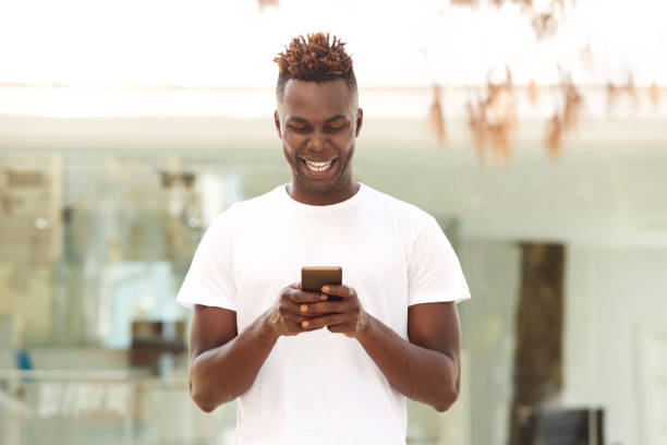 istock Smiling young afro american man using mobile phone standing outdoors in city 912334590