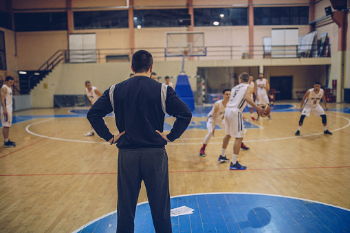 Coach watching group of male basketball players playing basketball