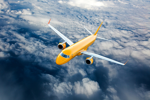 Orange airplane in flight. Passenger plane flying on a high altitude above the clouds.