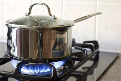 Close up color image depicting a cooking pan on a gas hob with blue flames in the kitchen.