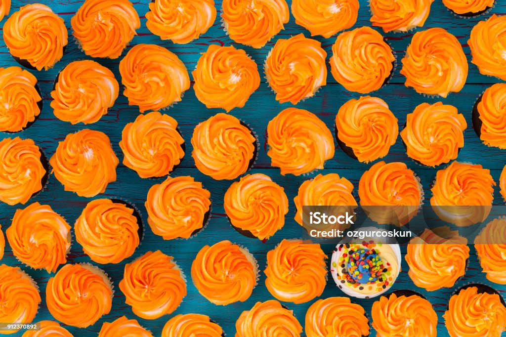 Background pattern of glazed orange cupcakes Background pattern of glazed orange cupcakes with one single different cookie with white icing and sprinkles viewed full frame from above in a conceptual image Standing Out From The Crowd Stock Photo