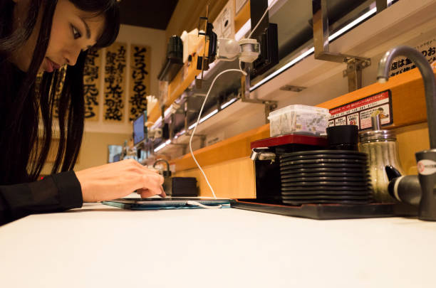 A woman who touches a touch pad with a sushi bar. A woman is manipulating the shop's touchpad at the sushi bar counter seat. kids eating tuna stock pictures, royalty-free photos & images