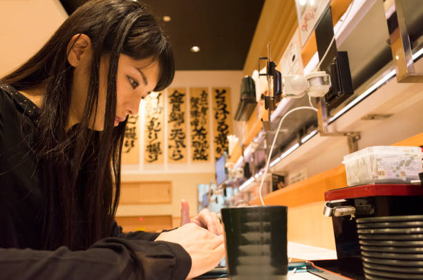 A woman who touches a touch pad with a sushi bar. A woman is manipulating the shop's touchpad at the sushi bar counter seat. kids eating tuna stock pictures, royalty-free photos & images