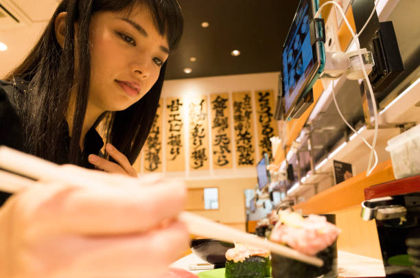 A woman eating sushi at a sushi bar. A woman is eating sushi at a counter seat of a sushi bar. kids eating tuna stock pictures, royalty-free photos & images