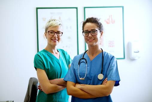 Retrato de dos enfermeros felizes con los eyeglasses de pie en la oficina con brazos cruzados una mirando a la cámara. photo
