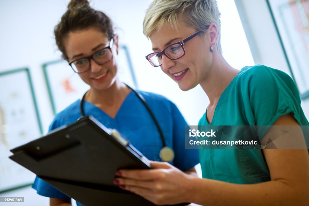 Vista ravvicinata di due infermieri professionisti con occhiali che controllano i documenti del paziente in un ufficio medici. - Foto stock royalty-free di Infermiere