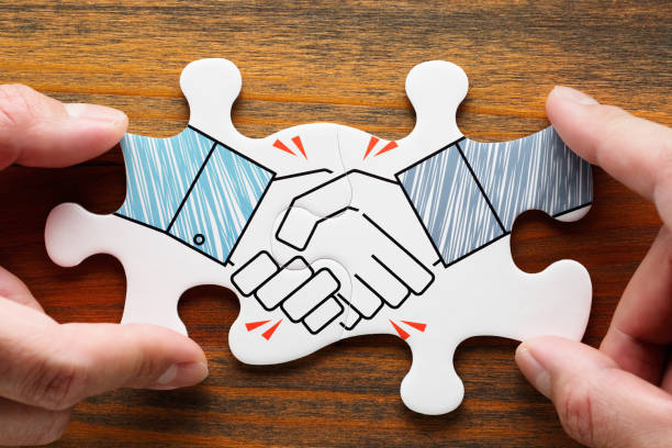 Putting together handshake jigsaw puzzle pieces on wood desk. stock photo