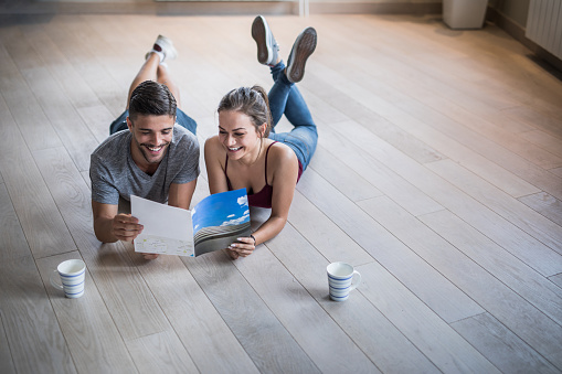 Young smiling couple reading catalogue while relaxing on the floor in their new apartment.