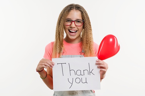 A teenage girl holding a paper with a thank you text, and a heart balloon, on a white studio background