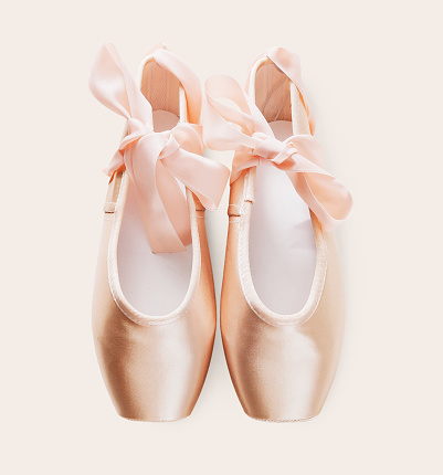 Pastel pink ballet shoes background. New pointe shoes with satin ribbon lay on white isolated backdrop