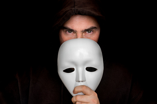 Mysterious man in black hiding his face behind white mask - anonymous concept