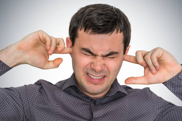 Man closes ears with fingers to protect from loud noise Man closes ears with fingers to protect from loud noise - excessive sound man closing ears photos stock pictures, royalty-free photos & images
