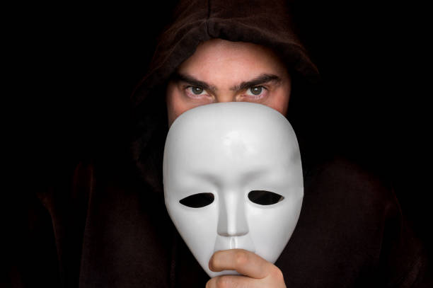 istock Mysterious man in black hiding his face behind white mask 912420846
