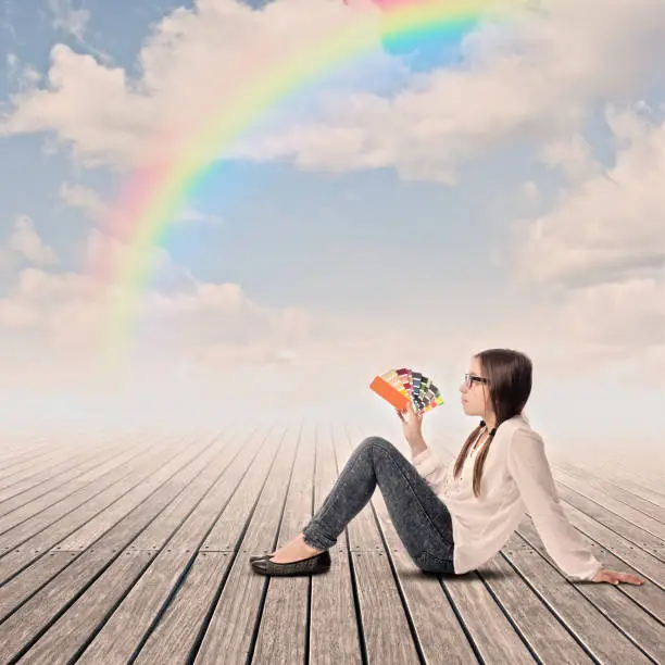 young girl holding a pantone palette on a wharf with rainbow in the sky