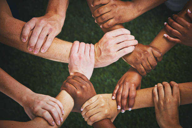 Many hands clasp wrists forming human chain Looking down at many mixed hands, each clasping the wrist of another person and forming an interlinked human chain or mesh. harmony photos stock pictures, royalty-free photos & images