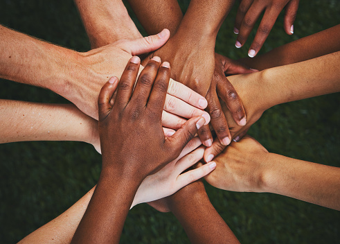 A large group of mixed unrecognizable people stretch out their arms and make a pile-up of their hands.