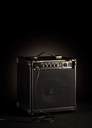 Black bass guitar amplifier whit a cord plugged in on black background