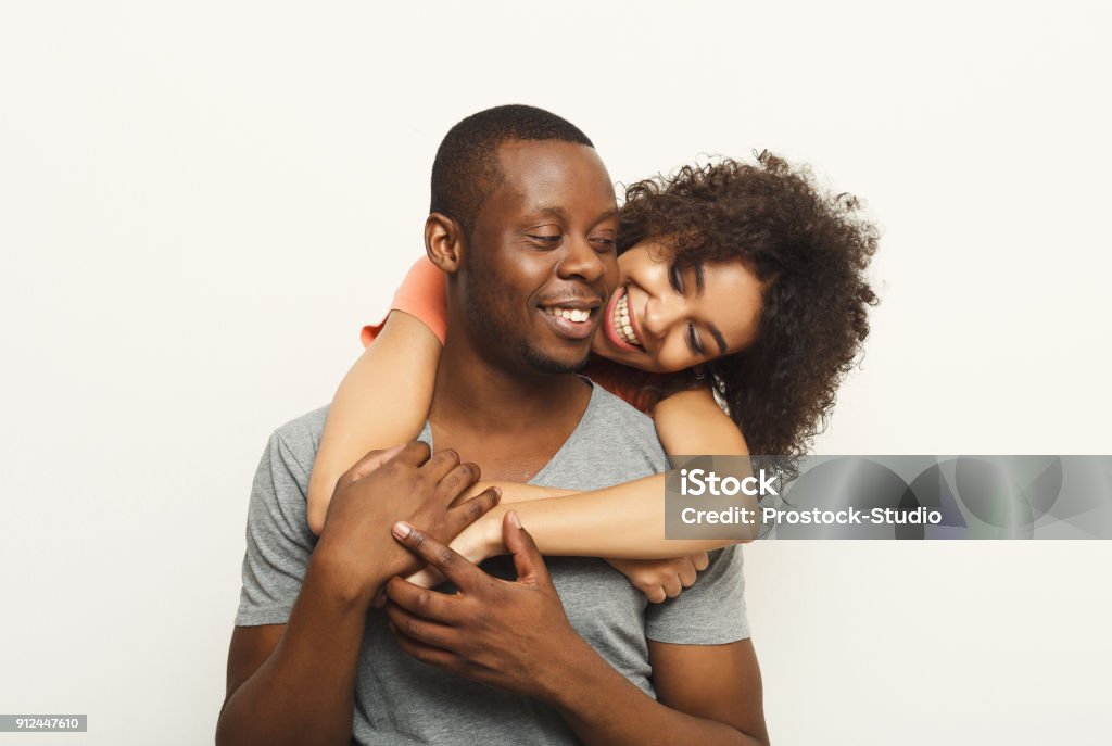 Black couple hugging and posing at white background Studio shot of happy casual african-american couple embracing, posing to camera and smiling on white studio background, copy space, isolated Couple - Relationship Stock Photo