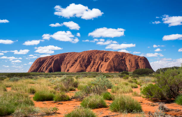 The Northern Territory, Australia - March 29, 2016: Fluffy clouds drift over Uluru (also known as Ayers Rock) in the Australian Outback. A genuine Wonder of the Natural World (and a UNESCO World Heritage Site), it's also a sacred place to the local Anangu people.