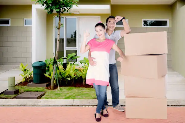 Happy couple showing OK sign while standing in front of their house with a pile of cardboard