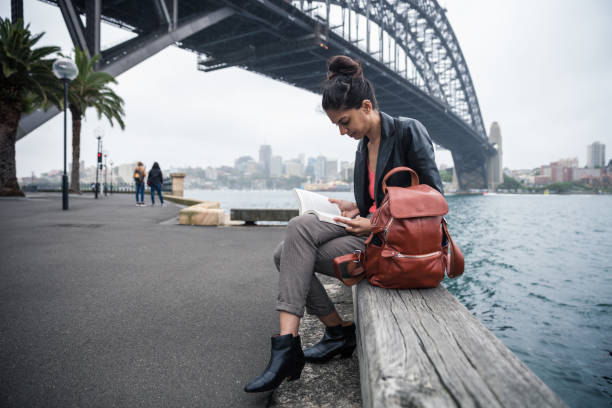 istock Woman reading a book sitting on a bench in Sydney Harbor 912457316