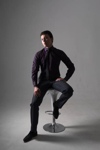 A young man in a business suit on a bar stool on gray background stock photo