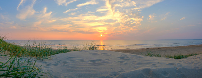View from the dunes on the sand beach of the North Sea shore on the coast line in The Netherlands during a beautiful summer sunset after a warm day in August.