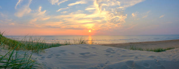 Summer sunset in the dunes at the North Sea Beach View from the dunes on the sand beach of the North Sea shore on the coast line in The Netherlands during a beautiful summer sunset after a warm day in August. north sea waves stock pictures, royalty-free photos & images