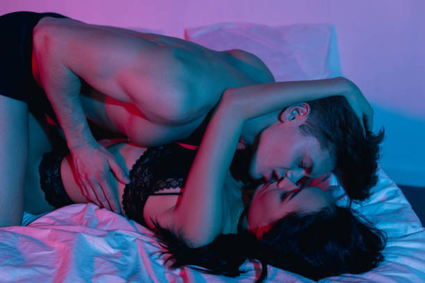 コンドームを押しベッドでカップルのキス - 官能 ストックフォトと画像