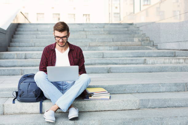 estudiante sonriente sentado en las escaleras usando laptop - smart casual fotos fotografías e imágenes de stock