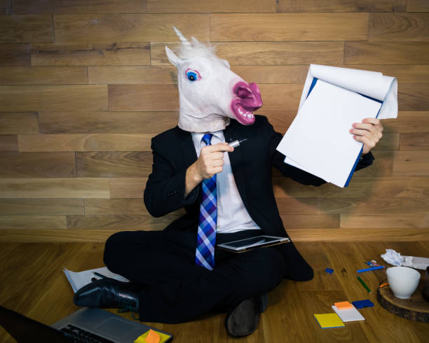 istock Unicorn in a suit and tie smiles and shows a white empty sheet 912501154