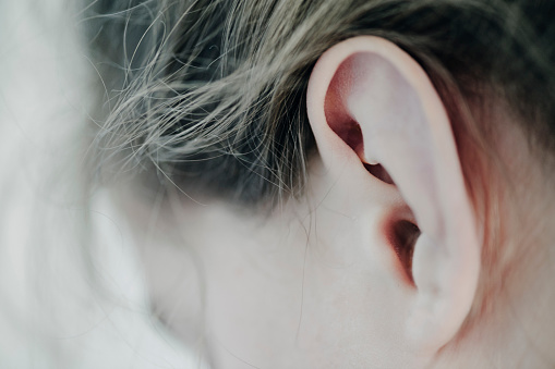 Delicate close-up of a young girl's ear, photographed with a very shallow depth of field with the point of focus on middle of the ear. Horizontal format with some copy space.