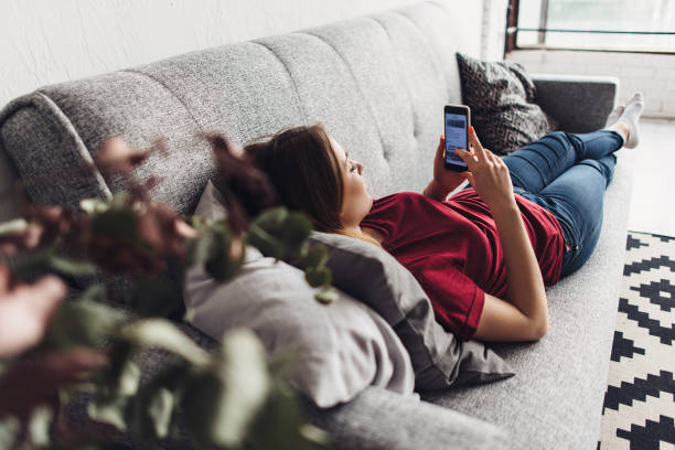 istock Young woman using smart phone while lying on the couch at home 912507618