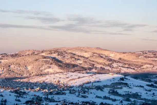 Koniakow village with snow covered meadows and hills above from Ochodzita hill in Beskid Slaski mountains in Poland during winter morning with blue sky