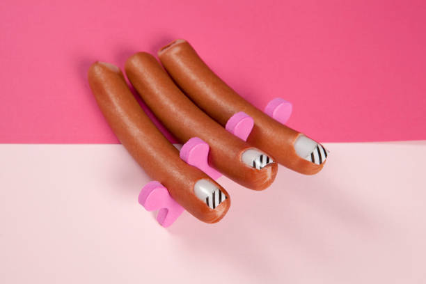 gradient pink background and sausage manicure 3 sausages with false nails placed in a manicure spacer like fingers on a bicolor pink background. Minimal funny and quirky pop still life photography hot dog photos stock pictures, royalty-free photos & images